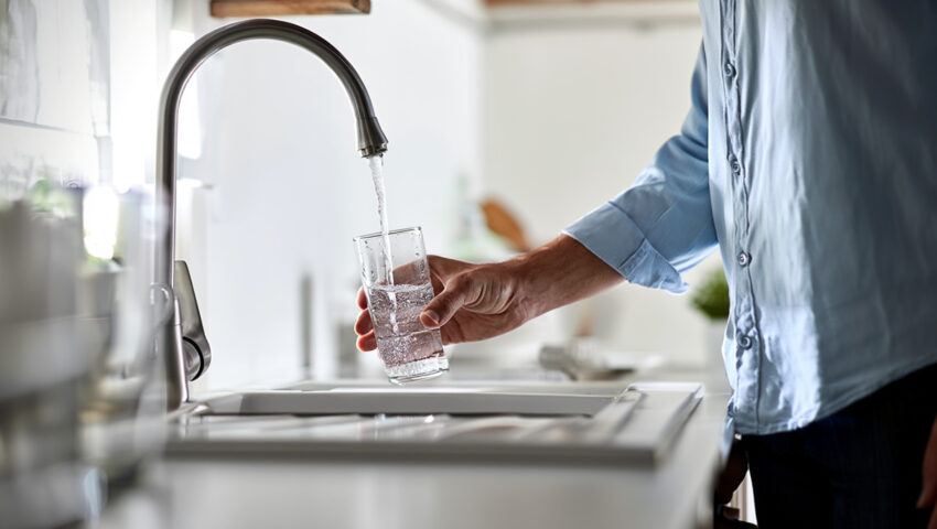A person fills a clear glass with tap water from a kitchen faucet