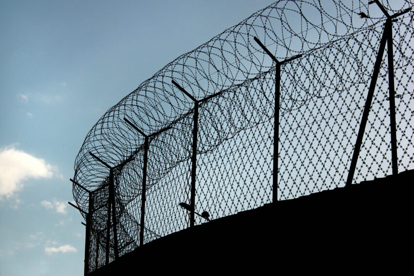 Coils of razor wire top a security fence, silhouetted against a cloudy sky