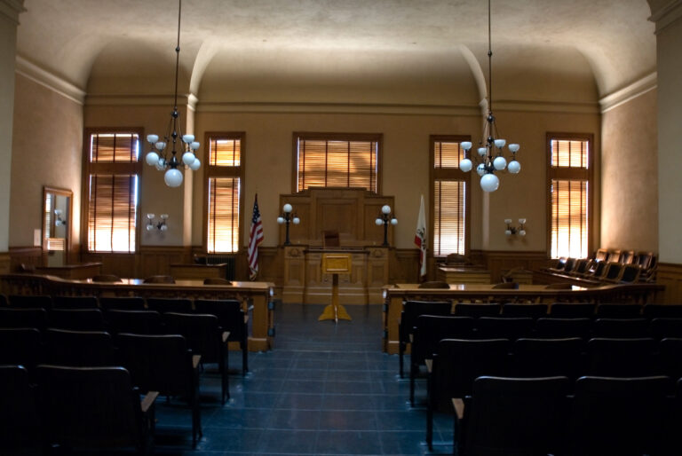 Empty courtroom with United States and California flags beside the judge bench