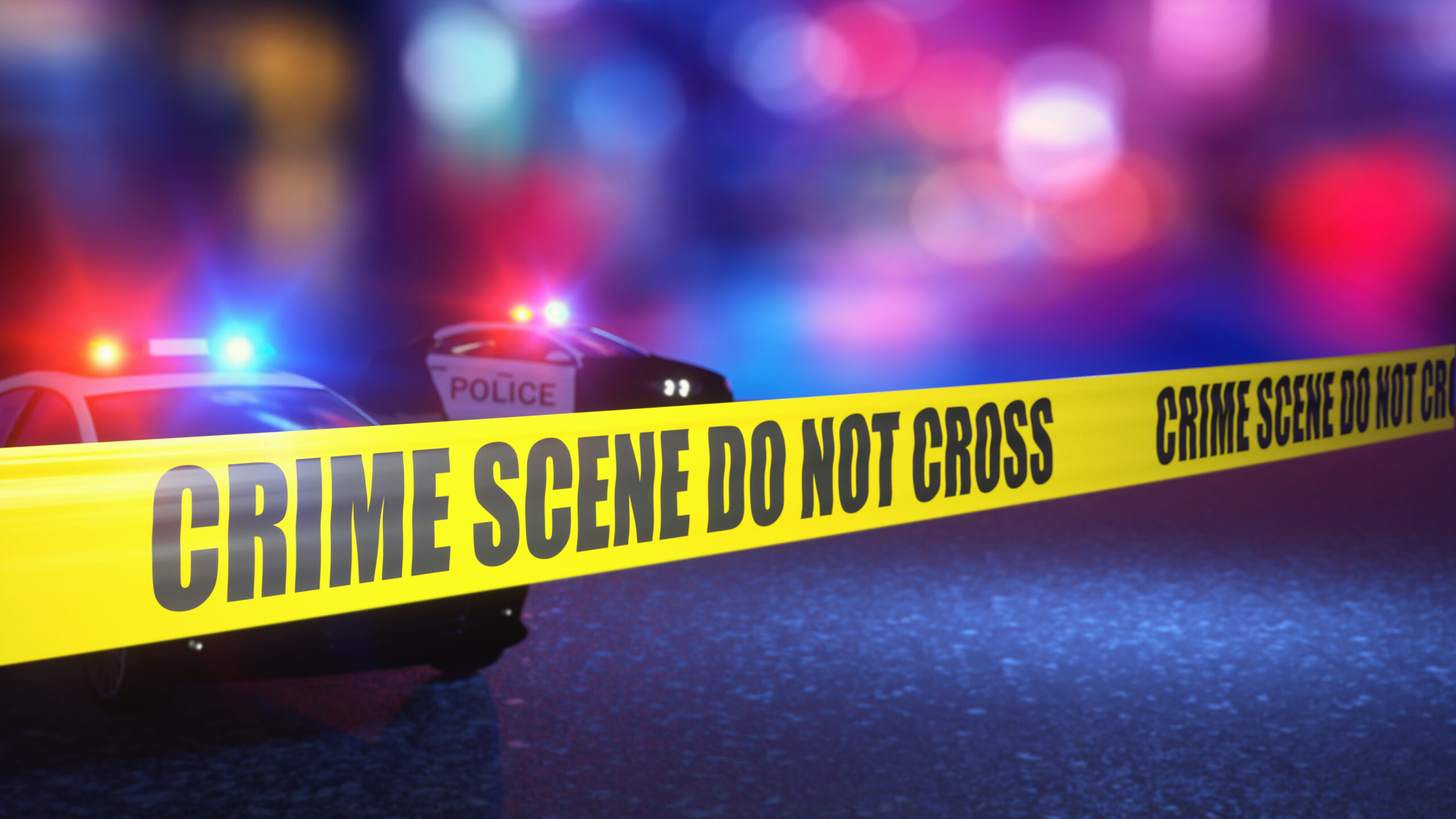 Yellow crime scene tape strung in front of a police vehicle at night