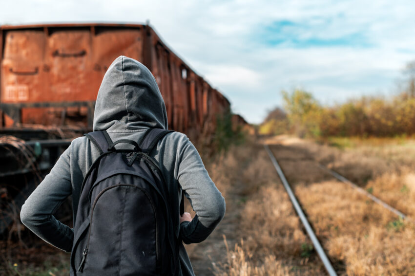 A person with a backpack walks away along railroad tracks past an old train car