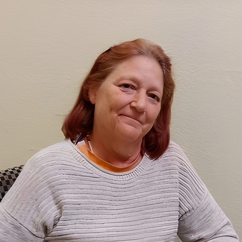 Renee Belinda Cooper, a woman with shoulder-length red hair in a gray sweater, seated against a beige wall