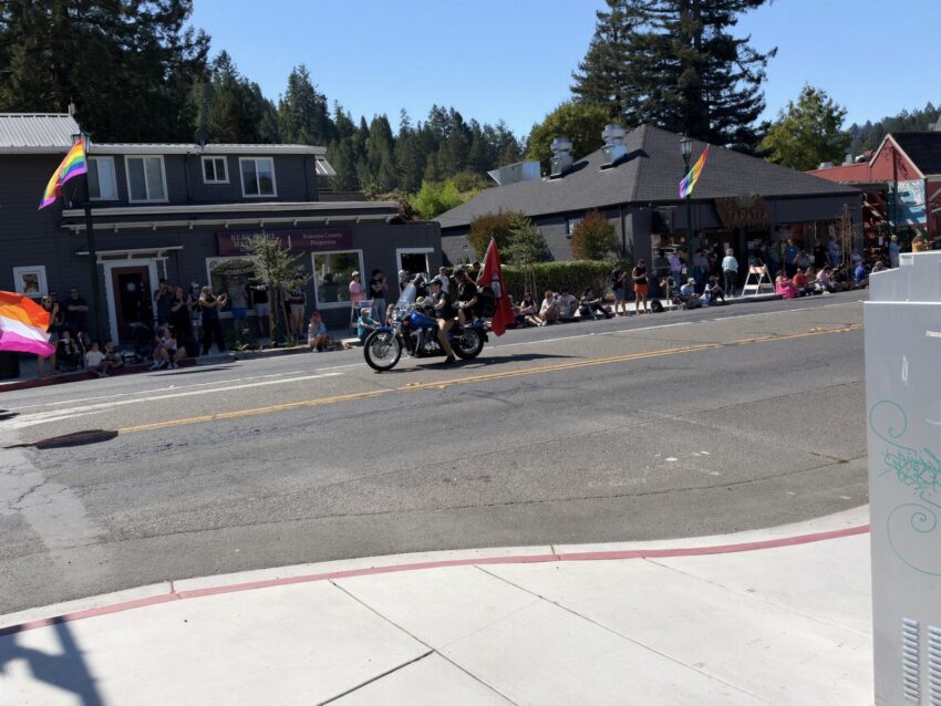 Motorcycle riders lead the Russian River Pride parade down Main Street in Guerneville past storefronts hung with rainbow flags
